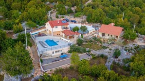 An aerial view of a property with multiple buildings, a swimming pool, and surrounding greenery. - House Jurica (Omis)