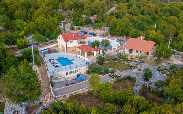 Vista aérea de una propiedad con varias edificaciones, piscina y vegetación circundante.