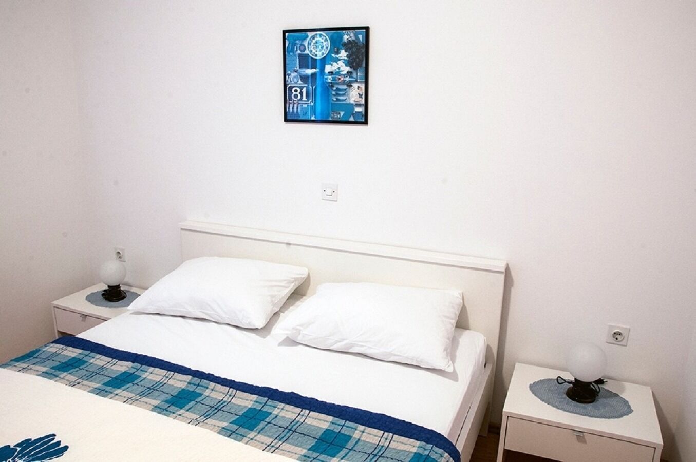 A simple, clean room with a bed, two bedside tables, and a wall-mounted picture.
