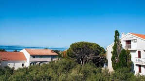 Una villa costera con techo de tejas rojas, rodeada de follaje y un cielo azul despejado.