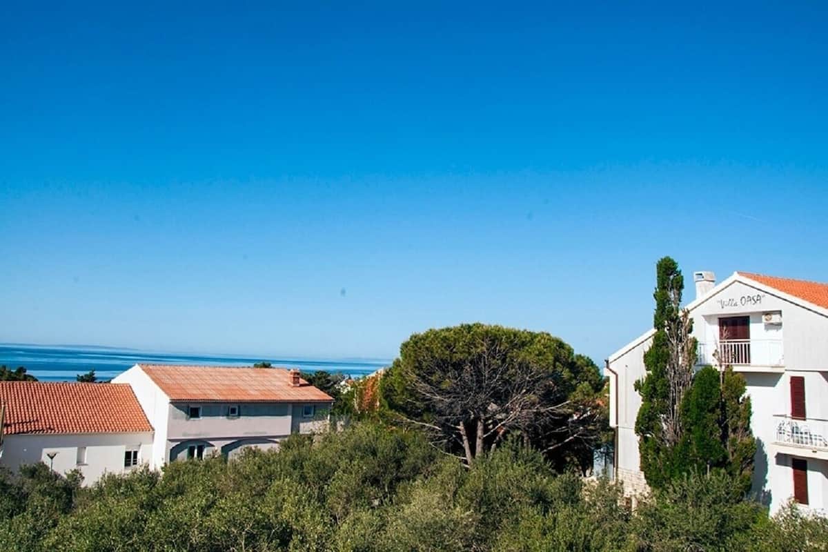 Uma vila costeira com telhado de telhas vermelhas, rodeada por vegetação e um céu azul límpido.