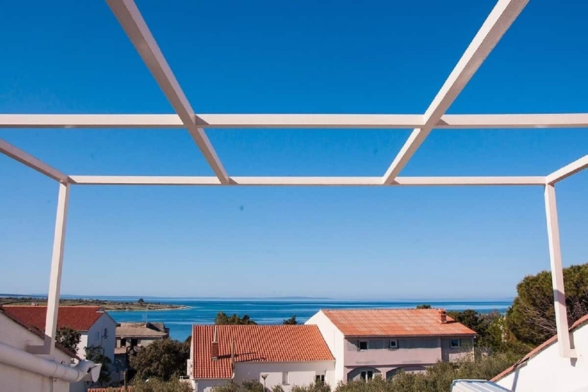 Vista através de uma varanda branca, com casas e céu azul límpido numa área costeira.