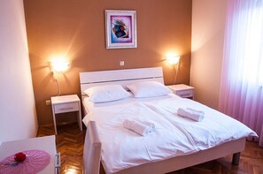 Una cama bien hecha con sábanas blancas y dos almohadas, una mesita de noche con una lámpara y un cuadro colgado en la pared.