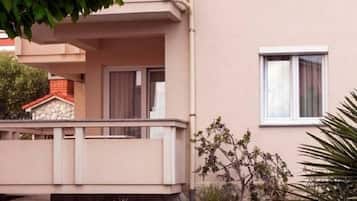 Ein zweistöckiges Gebäude mit einem Balkon, einem kleinen Garten und einem Baum im Vordergrund.