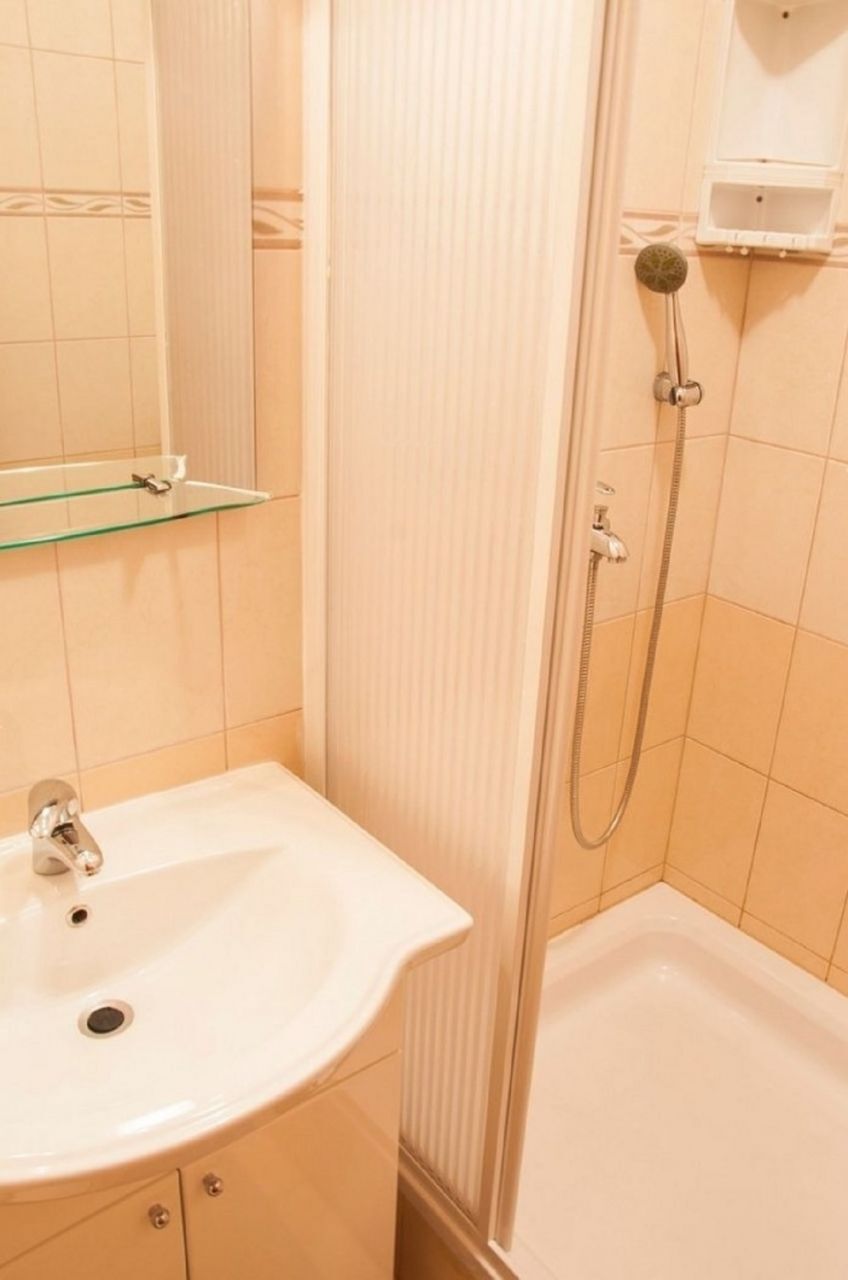 A bathroom with a sink, mirror, shower, and a glass shelf.
