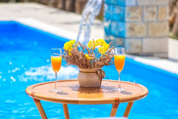 A poolside table with two glasses of orange juice and a vase of yellow flowers. - House Brist (Drnis)