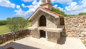 A stone-built outdoor kitchen with a chimney, surrounded by a stone wall and a paved patio. - House Brist (Drnis)