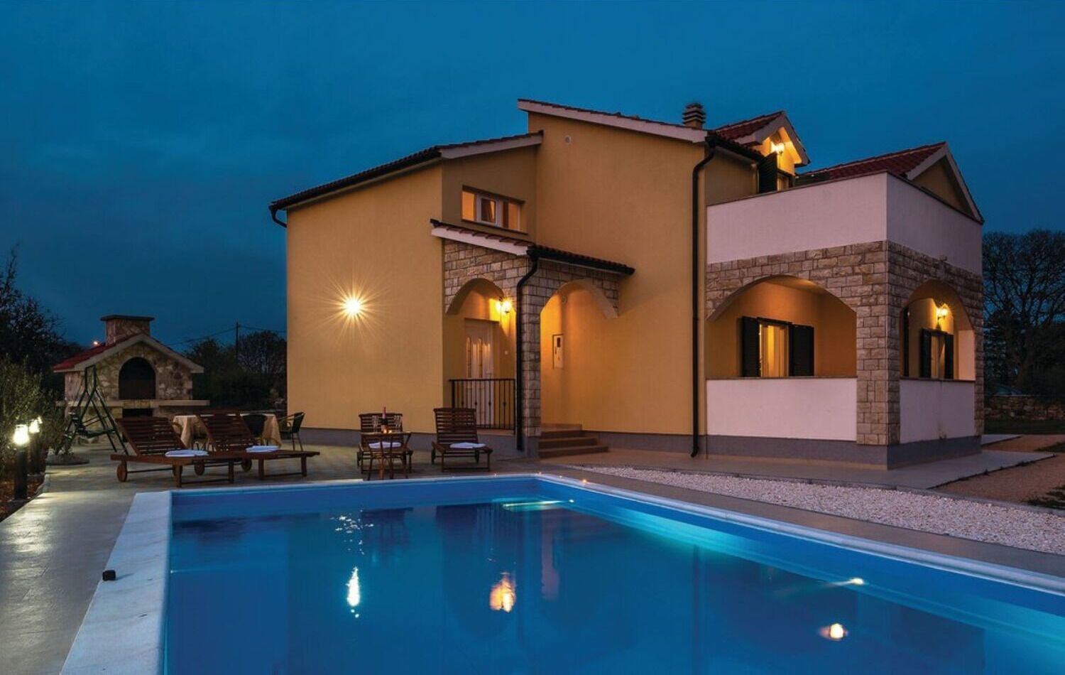 Une maison à deux étages dotée d’une piscine, d’un espace extérieur aménagé et de détails en pierre.