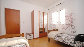 Ein Schlafzimmer mit zwei Betten, einem Kleiderschrank, einem Spiegel und einem Fenster mit blumigen Vorhängen.