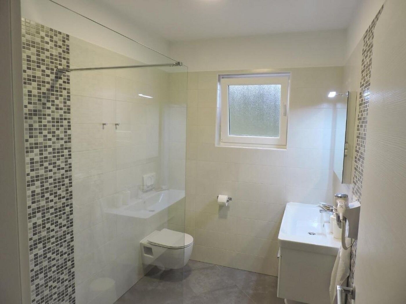 A small bathroom with a glass shower enclosure, a toilet, a sink, and a mirror.