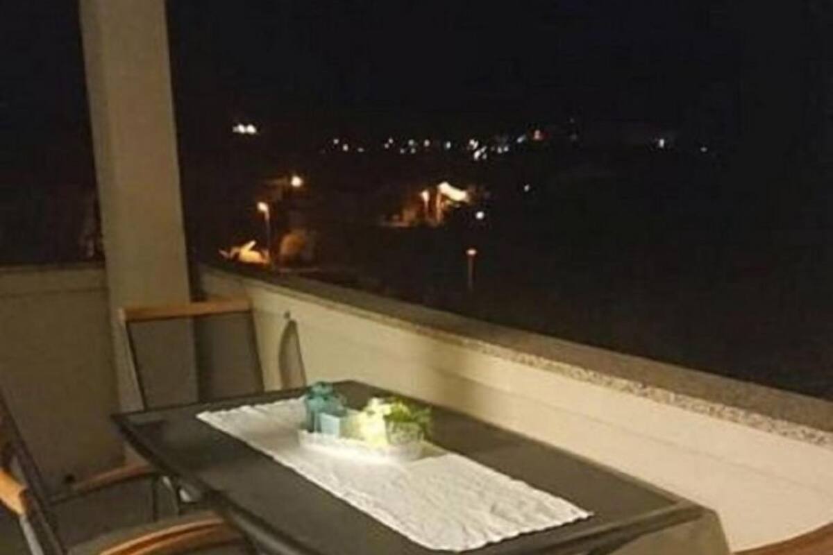 A balcony with a table and chairs, overlooking a cityscape at night.
