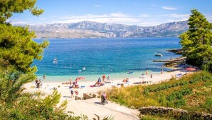 Ein Strand mit klarem, blauem Wasser, badenden Personen und Booten.