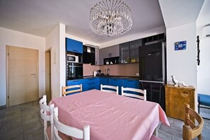 A modern kitchen with blue cabinets, a dining table with a pink tablecloth, and a chandelier. - Apartment Afitojen (Postira)