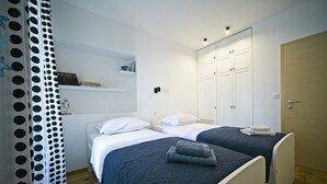 Een slaapkamer met twee bedden, een kledingkast en een plank met boeken.