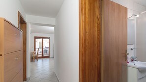 A hallway with wooden cabinets, a white tiled floor, and a bathroom with a sink and mirror. - Apartments Marijan (Pakostane)