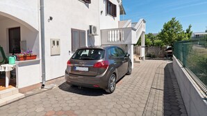 A car parked in a driveway of a white building with a balcony and an air conditioning unit. - Apartments Marijan (Pakostane)