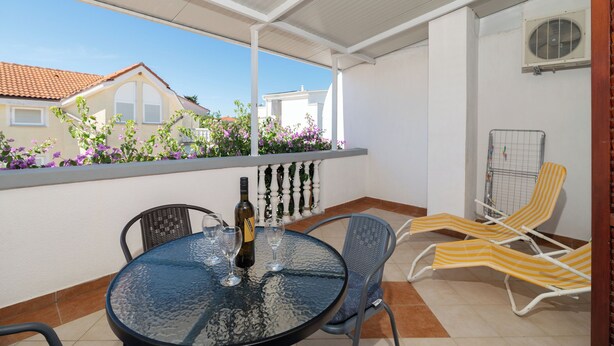 A covered outdoor area with a table, chairs, and a bottle of wine. - Apartments Marijan (Pakostane)