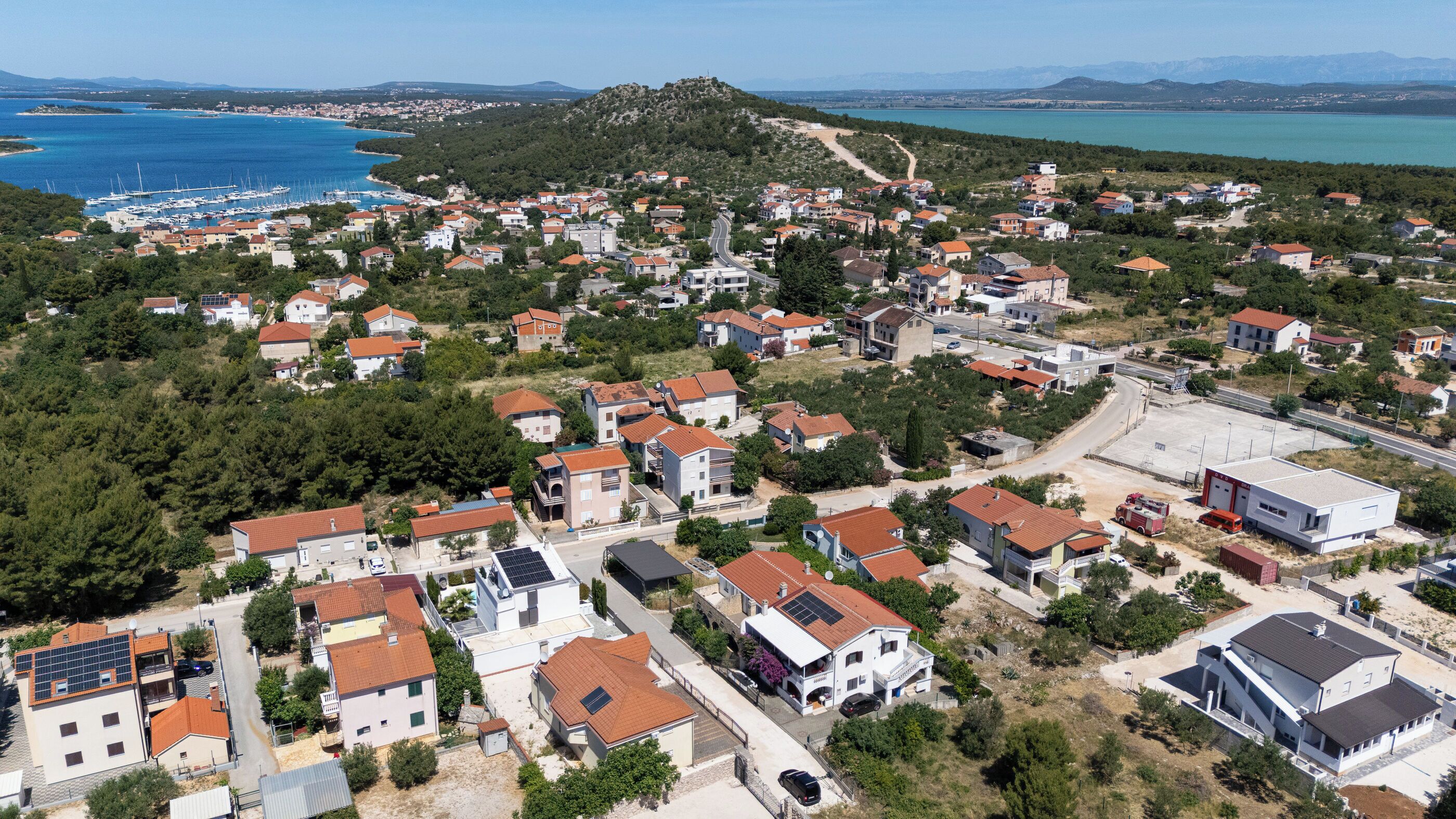 A residential area with houses, a road, and a body of water in the background.