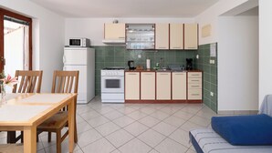 A compact kitchen with a dining area, a stove, a microwave, and a refrigerator. - Apartments Marijan (Pakostane)