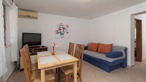 A living room with a dining table, chairs, a television, a sofa, and a painting on the wall. - Apartments Marijan (Pakostane)