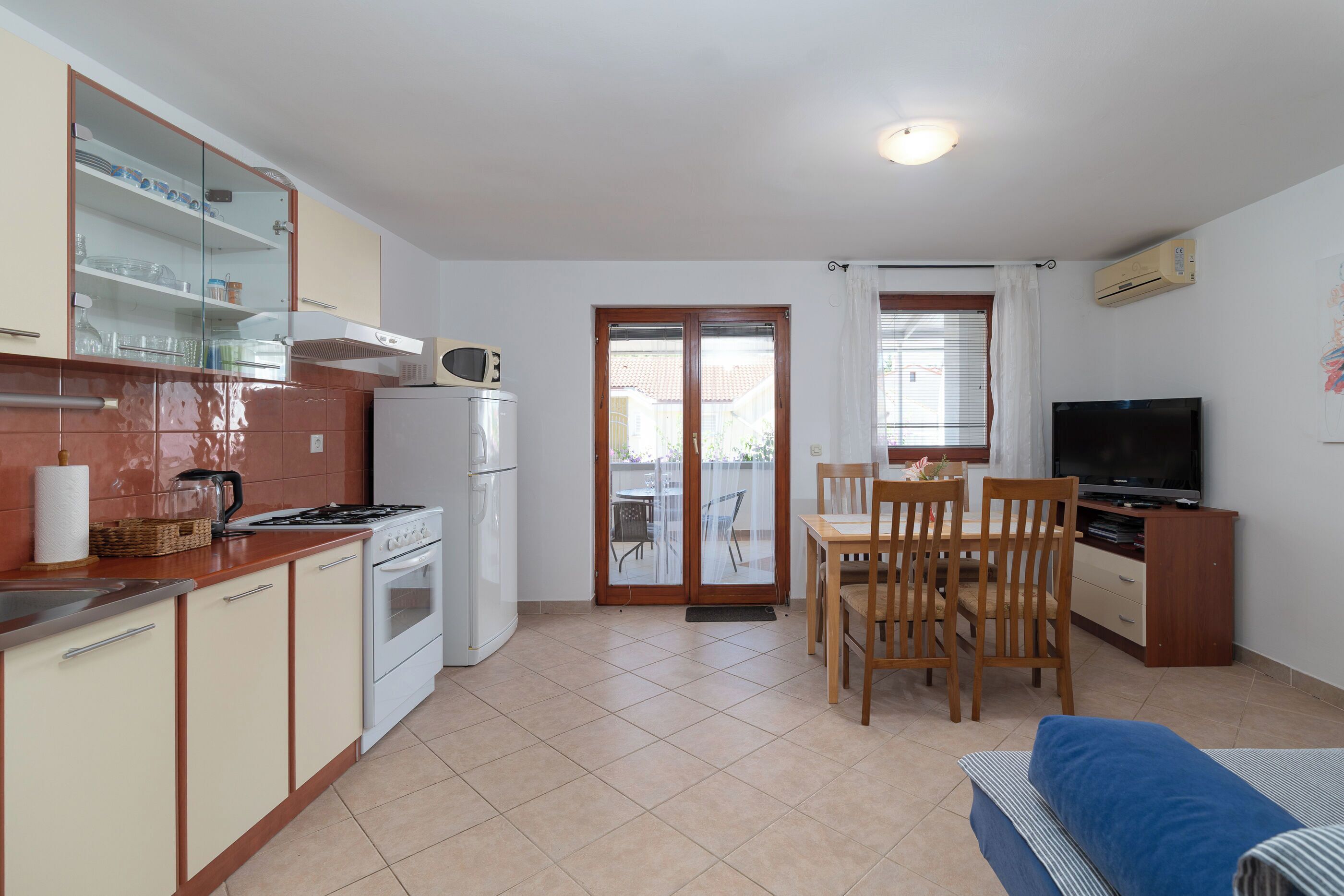 A compact kitchen with a stove, microwave, and refrigerator, a dining area with a table and chairs, and a television.