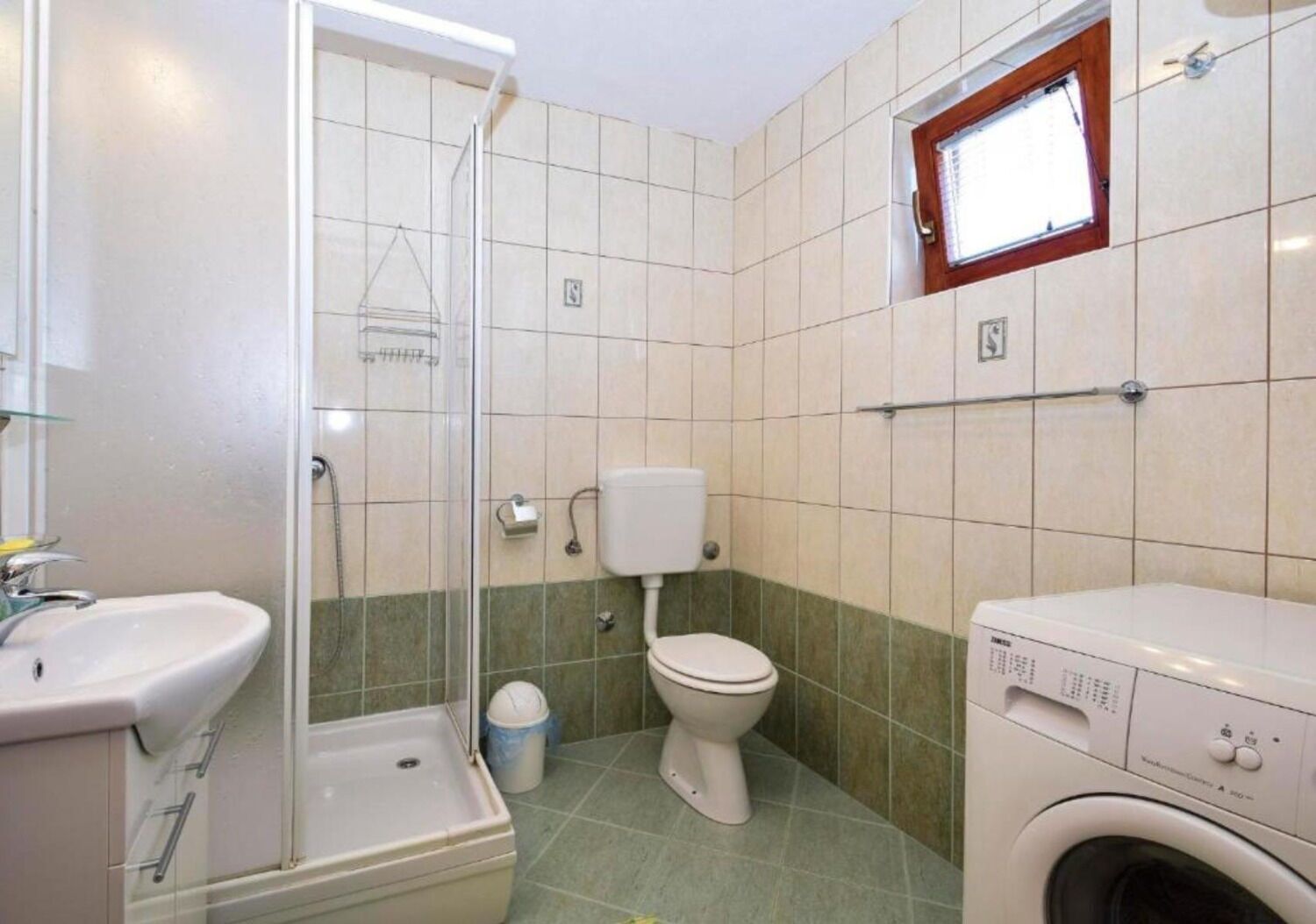 A bathroom with a shower, toilet, sink, and washing machine.