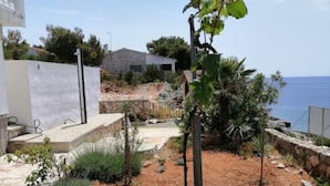 Ein Garten mit einem Kiesweg, der zu einem weißen Gebäude führt, umgeben von viel Grün und Blick aufs Meer.