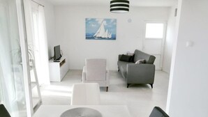 Ein modernes Wohnzimmer mit einer Couch, einem Esstisch mit Obstschale und einem Segelbootgemälde an der Wand.