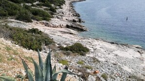 Eine Küstenlandschaft mit felsigem Gelände und spärlicher Vegetation, die zu einem ruhigen Meer führt.
