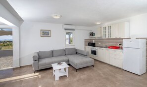A modern kitchen with a grey sofa, a small white table, and a view of the outdoors. - House Nane Garden (Supetar)