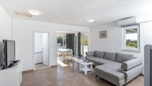 A modern living room with a grey sofa, a flat-screen TV, and a dining area with a table and chairs. - House Nane Garden (Supetar)