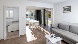 A modern living room with a grey sofa, a white coffee table, and a dining area with a white table and chairs. - House Nane Garden (Supetar)