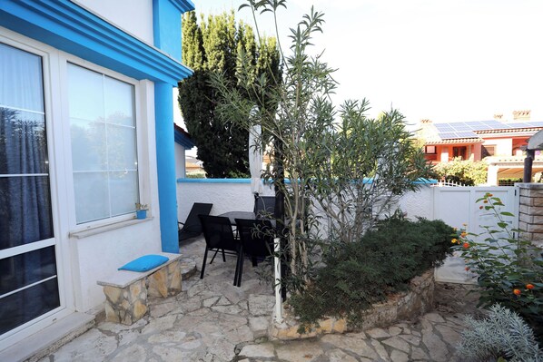 Une terrasse en pierre avec une table et des chaises, un petit banc et une plante en pot.
