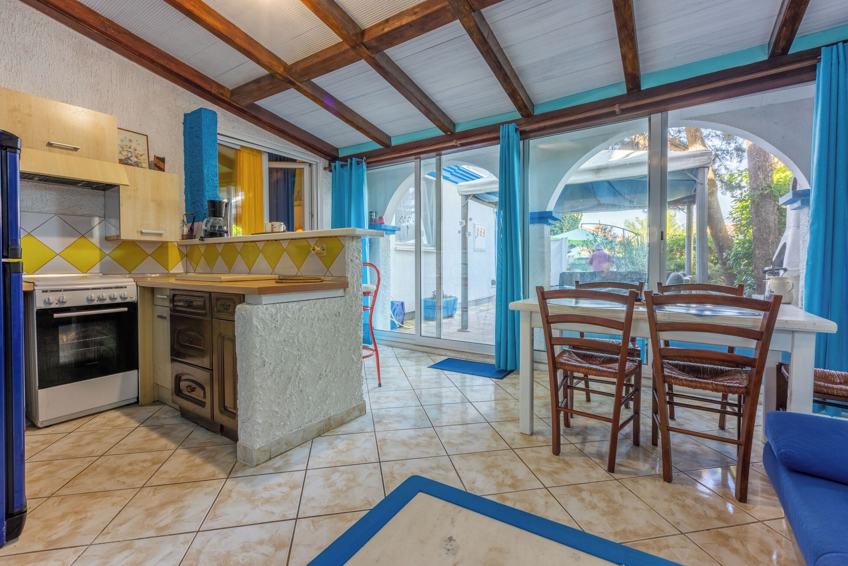 A kitchen with a built-in oven, a coffee maker, and a dining area with wooden chairs and a table.