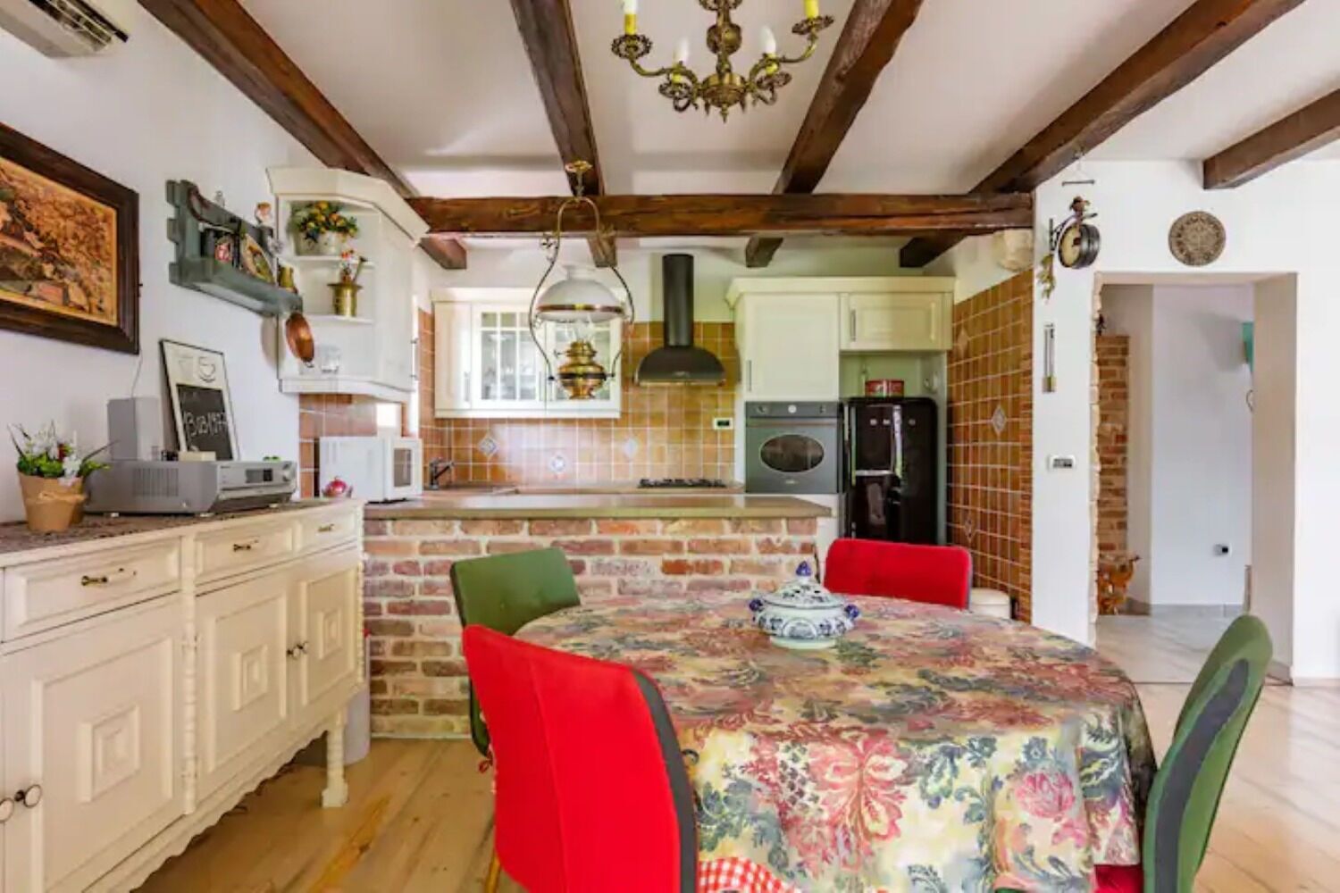 A kitchen with a brick island, white cabinets, and a dining table with red chairs.