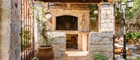 Un espacio al aire libre de piedra con una rústica chimenea de piedra, plantas en macetas y una reja de metal.