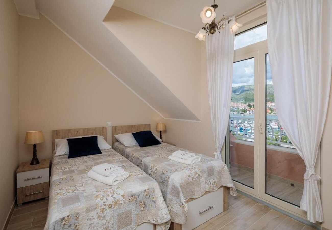 A bedroom with two beds, a nightstand, and a view of a cityscape through a sliding glass door.