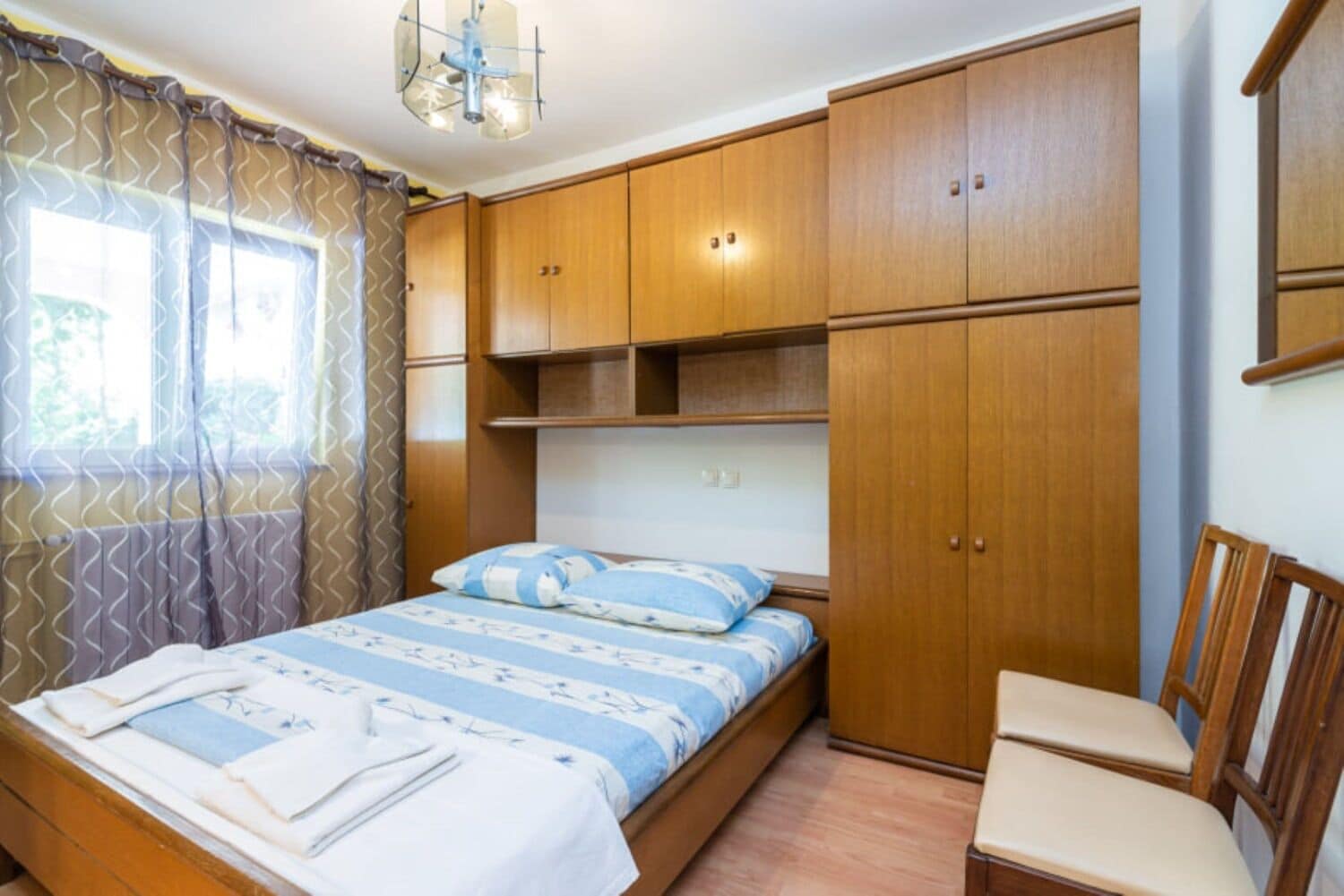 A bedroom with a bed, wooden wardrobe, and a chair.