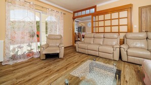 Ein Wohnzimmer mit einem beigen Sofa, zwei Sesseln, Holzboden, einem Glastisch und einer Holzwand.