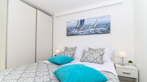 Una camera da letto con un letto, cuscini, un comodino, una lampada e un quadro raffigurante barche a vela.