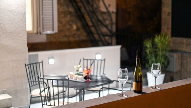 Zona pranzo con tavolo e sedie, una bottiglia di vino e due bicchieri da vino su un balcone.