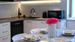 Una cucina moderna con mobili bianchi, un forno a microonde e una zona pranzo apparecchiata con piatti, bicchieri e un vaso con fiori rosa.