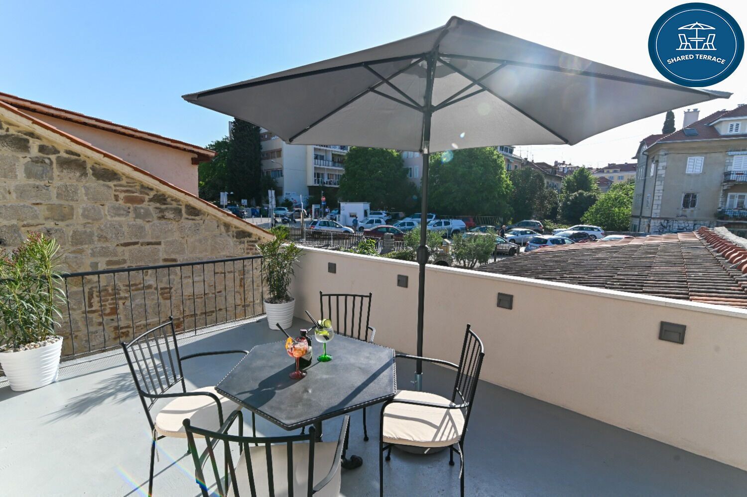A terrace with a table and chairs, a large umbrella, and potted plants.