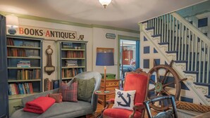 A cozy room with a bookshelf labeled 'BOOKS ANTIQUES', a red armchair, a wooden rocking chair, and a staircase with blue accents. - Hospitality as Sweet as Apple Pie! (Stonington)