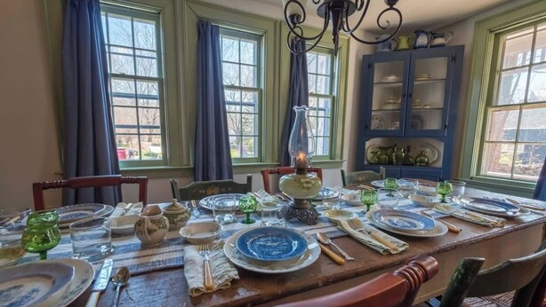 A dining room with a long table set for a meal, featuring a chandelier, blue and white plates, and a cabinet in the background. - Hospitality as Sweet as Apple Pie! (Stonington)