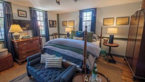 A traditional bedroom with a four-poster bed, a wooden dresser, a small table with a lamp, and a wardrobe. - Hospitality as sweet as apple pie! (Stonington)