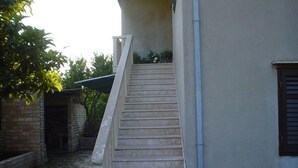 Un escalier menant à l’entrée d’un immeuble, entouré d’une cour pavée de pierres et de verdure.