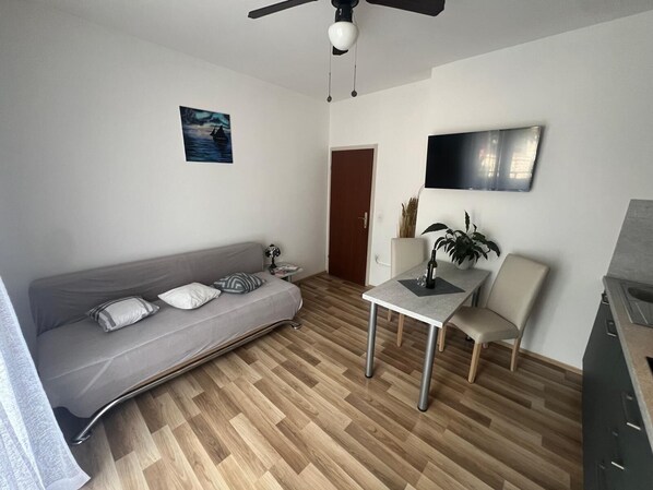 A modern living room with a grey sofa, a small table with a bottle, a chair, a TV mounted on the wall, and a wooden floor. - Apartment Neri (Supetar)