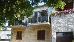 Un bâtiment à deux étages, doté d’une façade en pierre, d’un balcon avec une rambarde en métal et d’une jardinière ornée de fleurs roses.
