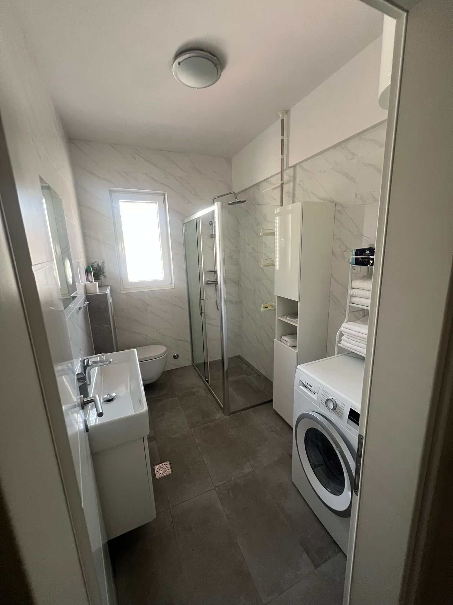 Une salle de bain moderne dotée d’une douche à parois de verre, d’un lavabo encastré et d’un lave-linge à chargement frontal.